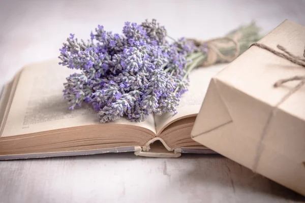 Lavender bouquet laid over  an old book and a wrapped gift box on a white wooden background. Vintage style.