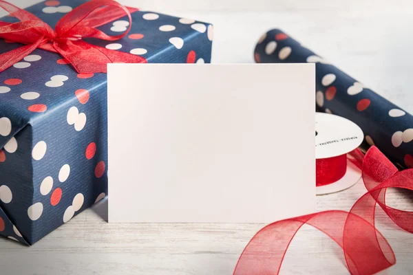 Empty greeting white card. Wrapped gift and wrapping materials over a white wood background. Vintage style.