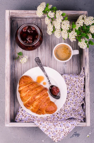 Top view of fresh croissant with strawberry jam and coffee cup  on vintage rustic tray. Breakfast concept. Toned image