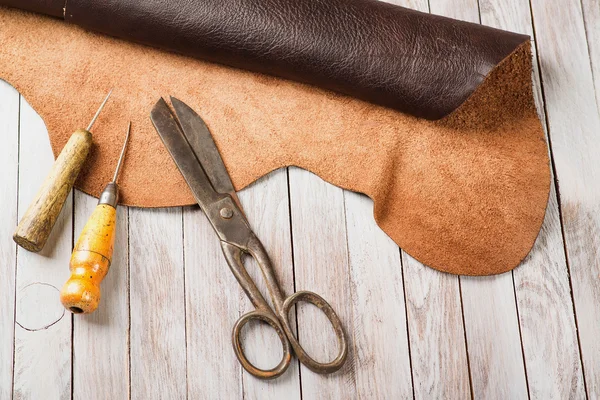 Leathersmith\'s work desk . Pieces of hide and leather working tools on a work table.