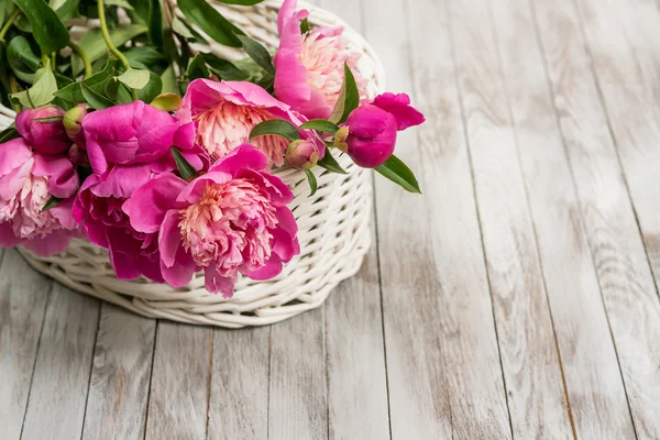 Beautiful flowers peonies in basket on light wooden background.