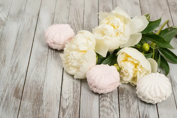 Beautiful white peonies flowers and marshmallows on white wooden background.