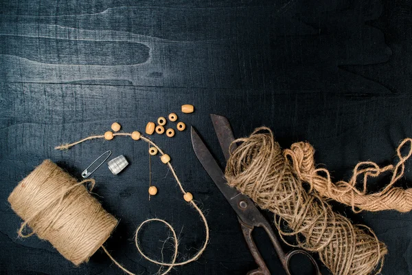 Set for needlework: scissors and skein jute twine on black background. Top view.