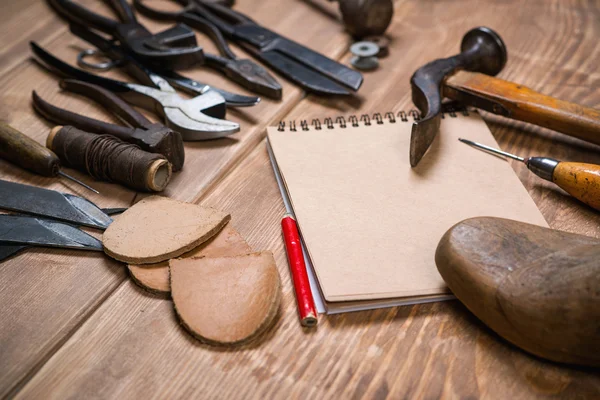 Set of tools, notebook, pencil for shoemaker on a wooden background.