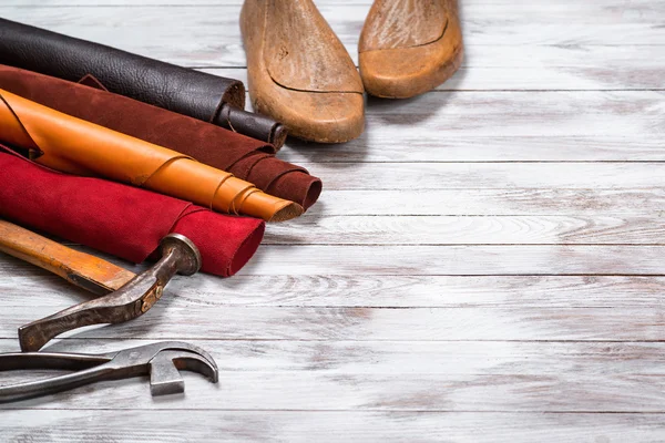 Brightly colored leather in rolls, working tools and shoe lasts on white wooden background. Leather craft. Copy space.
