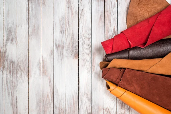 Brightly colored leather in rolls on white wooden background. Leather craft. Copy space. Top view.