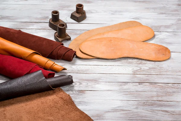Set of leather in rolls, craft tools on white wooden background. Workplace for shoemaker. Working handmade tools on a work table.
