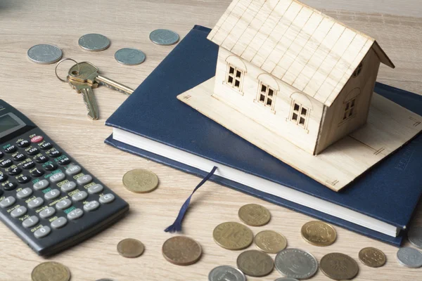 Home savings, budget concept. Model house, notepad, pen, calculator and coins on wooden office desk table.