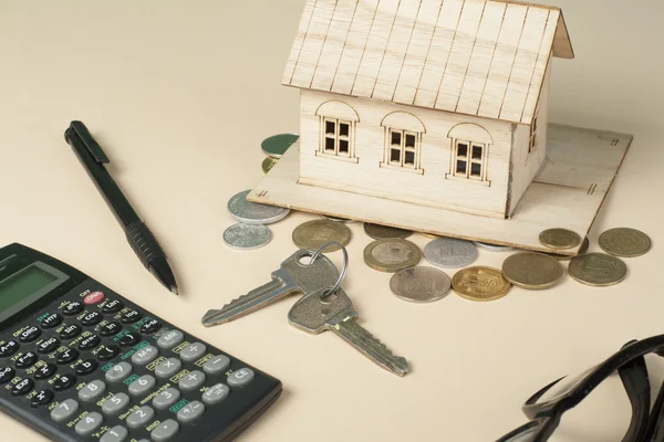 Home savings, budget concept. Model house, notepad, pen, calculator and coins on wooden office desk table.