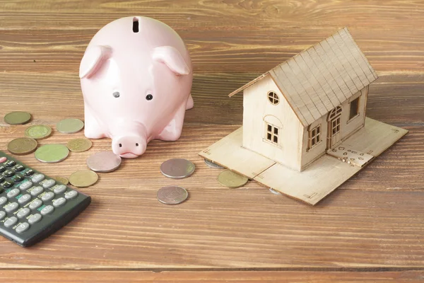 Home savings, budget concept. Model house, notepad, pen, calculator and coins on wooden office desk table.