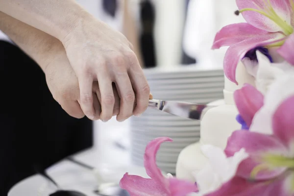 Cutting wedding cake with pink flowers