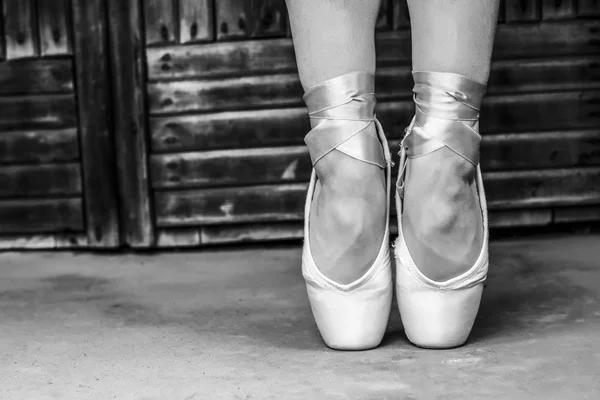 Feet dressed in dance pointe shoes and sports shoes. Black and white photo