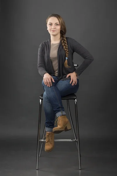 Woman sits on a high chair on gray background