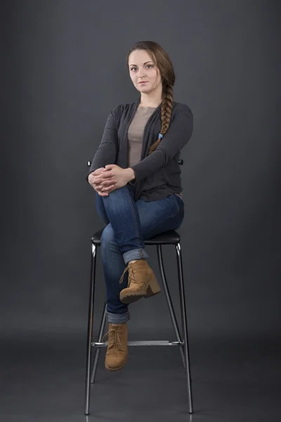 Woman sits on a high chair on gray background