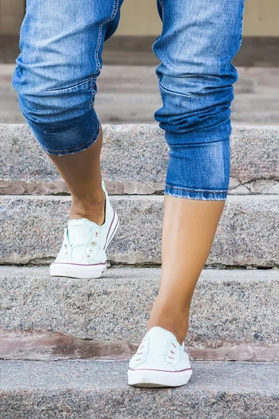 Feet dressed in dance pointe shoes, sports shoes on the background of stone steps. Sexy female legs