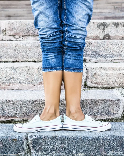 Feet dressed in dance pointe shoes, sports shoes on the background of stone steps. Sexy female legs