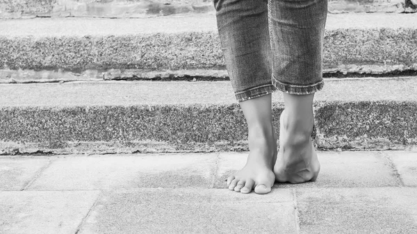Barefoot dancer foot in jeans and a foot on the background of stone steps. Sexy female legs. Black and white photo