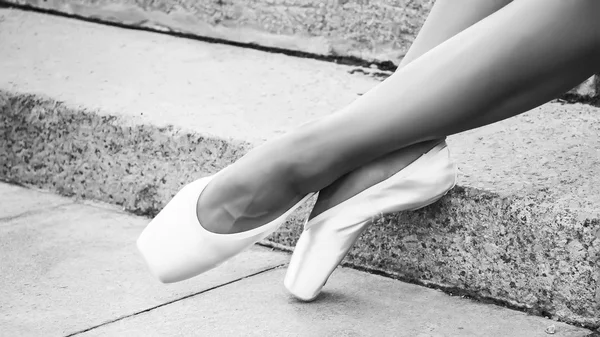 Feet dressed in dance pointe shoes, sports shoes on the background of stone steps. Sexy female legs. Black and white photo
