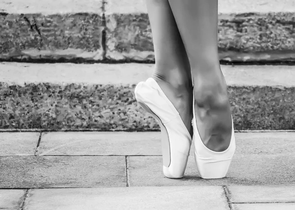 Feet dressed in dance pointe shoes, sports shoes on the background of stone steps. Sexy female legs. Black and white photo