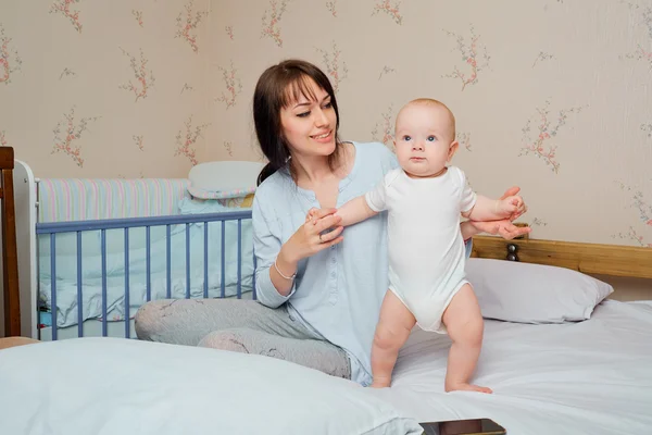 Mother and baby on the bed holding hands, playing. Mum learns th