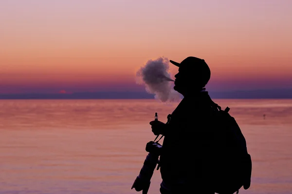 Silhouette of man smoking a pipe in cap at sunset. Photographer