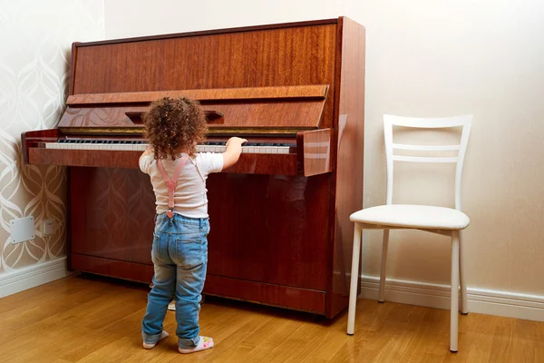 Back view. A child stands in front of the piano and plays a melo