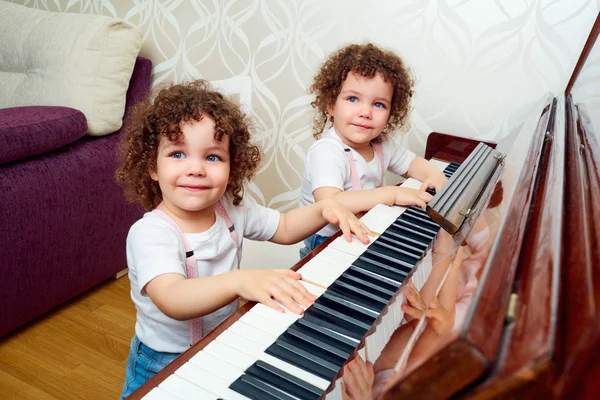 Two funny twin playing the piano together, smiling, laughing. Ch