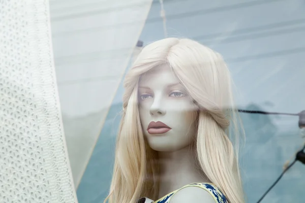 Cute realistic female mannequin face close-up in a shop window. Beautiful Caucasian manikin head with blonde hair