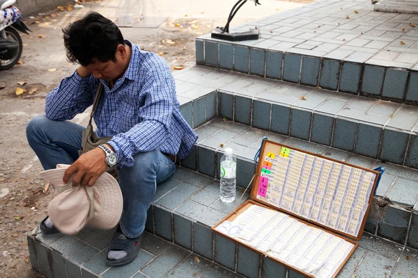 Pattaya, Thailand - March 28, 2016: Tired lottery seller sitting on a street selling cheap raffle tickets