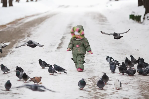 Child runs through a flock of pigeons on the square in winter city park