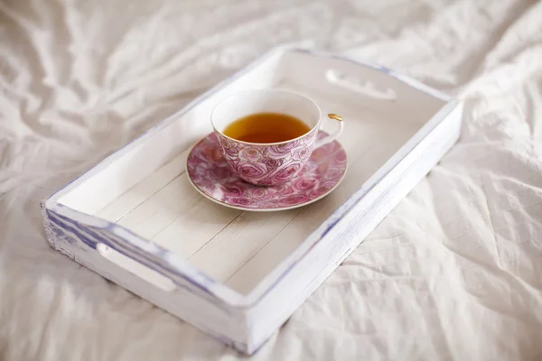 Wooden tray with cup of tea on the bed