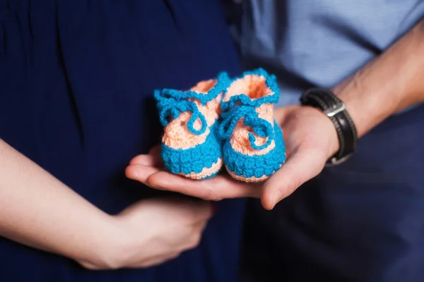 Cute blue knitted baby booties on hands. Pregnancy concept
