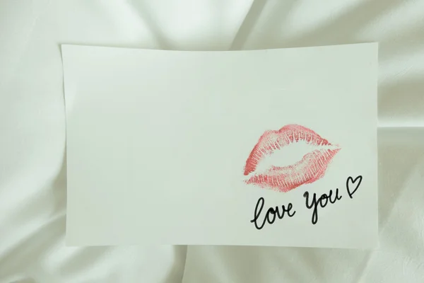 Red lips kiss love you write on white note on white bed