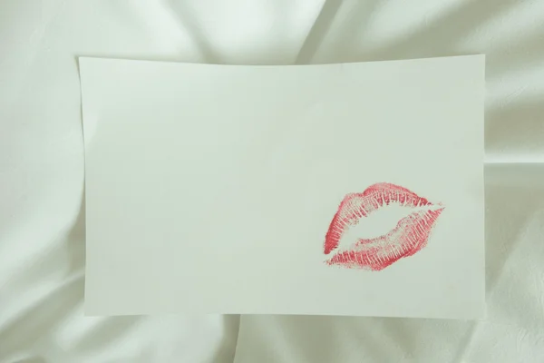 Red lips kiss on white note on white bed