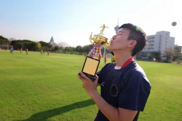 Asia football player man kiss trophy, celebrate his winner champion of soccer sport game in green field.