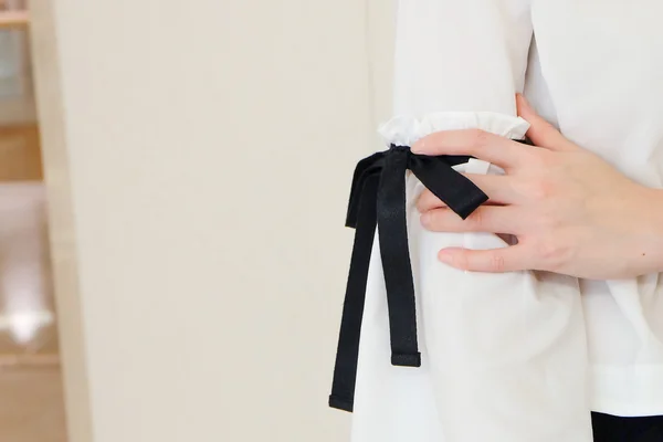 Woman hand on long white sleeve with black string bow tie style details. Close up trendy fashion.