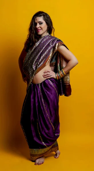 The young dark-haired woman in a beautiful Indian saris and colorful bracelets posing barefoot putting her hands on waist. Indian style.