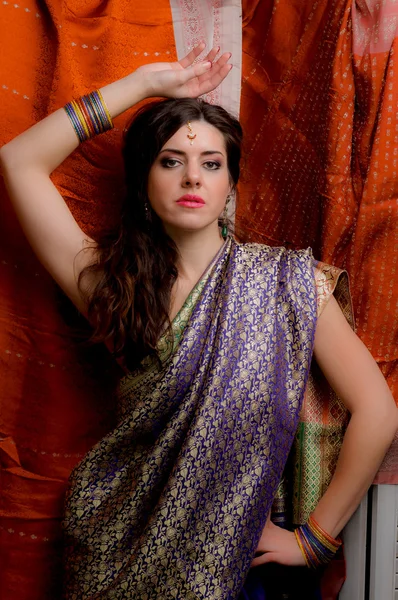 The young dark-haired woman in the rich Indian sari looks thoughtfully holding up one arm above the head. Indian style.
