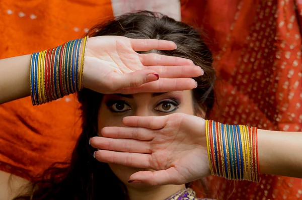 The young dark-haired woman in Indian sari and colorful bangles  looking through his hands. Indian style.