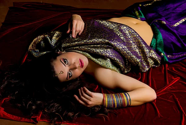 Young woman with flowing hair dressed in beautiful Indian sari lies on the background of bright red velvet. Indian style.