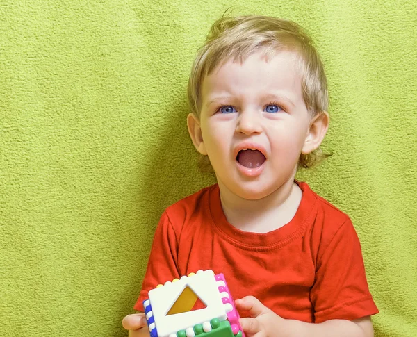 Little blond boy with blue eyes is holding a bright cube,  taking his mouth is widely to indignant shouts