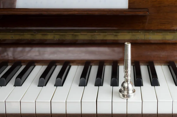 A trumpet mouthpiece upon the piano keys, close up