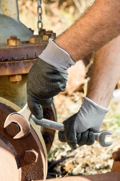 Hands with Work Gloves Holding a Wrench and Tighten very Rusty Bolts