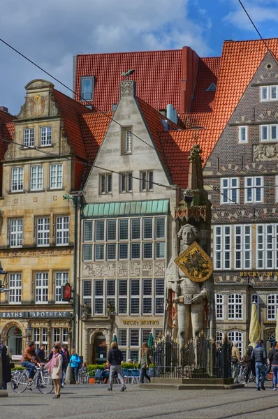 Tourists walking and standing on the main market square with the famous statue of \'Roland of Bremen\' and historic houses in the background.