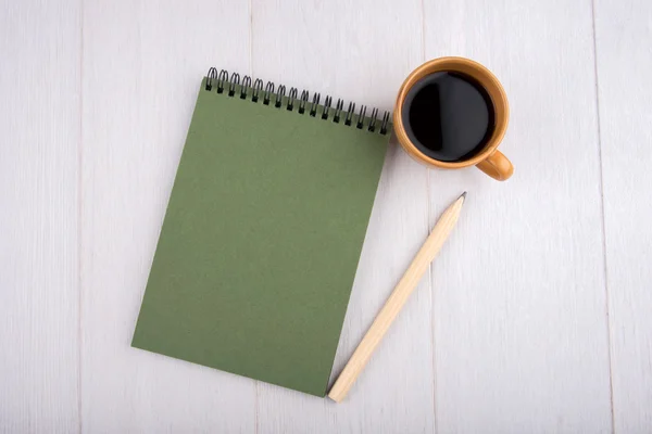 Cup of coffee, green notebook, pencil, overhead view