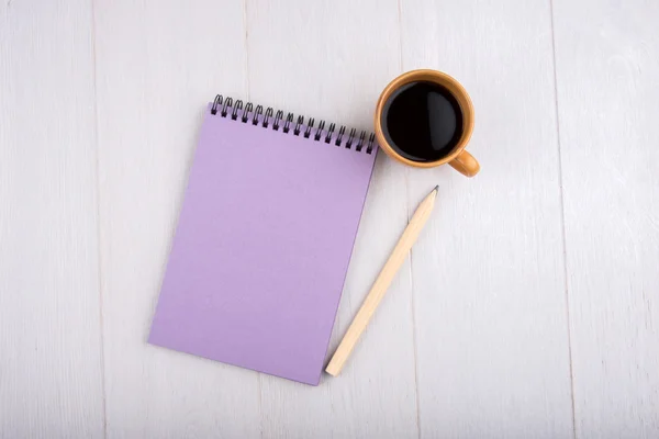 Cup of coffee, purple notebook, a pencil, top view