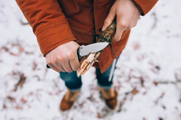 A man uses a knife to whittle a stick out hiking