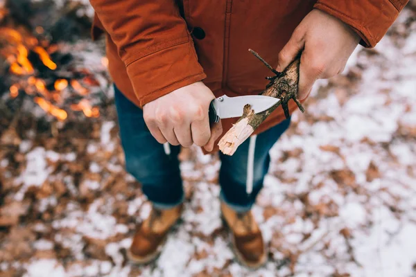 A man uses a knife to whittle a stick out hiking