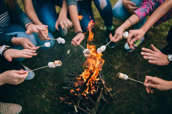 Sticks with marshmallows above campfire