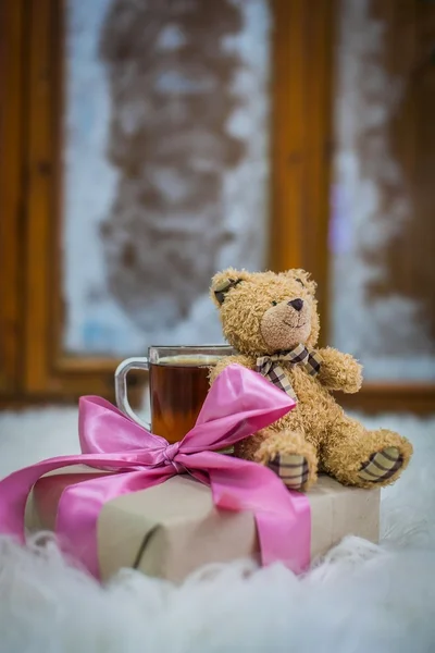 Toy bear and gift on the background of a frosty window and hot tea